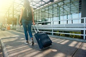 A woman walks with a suitcase outside an airport terminal, ready for travel.