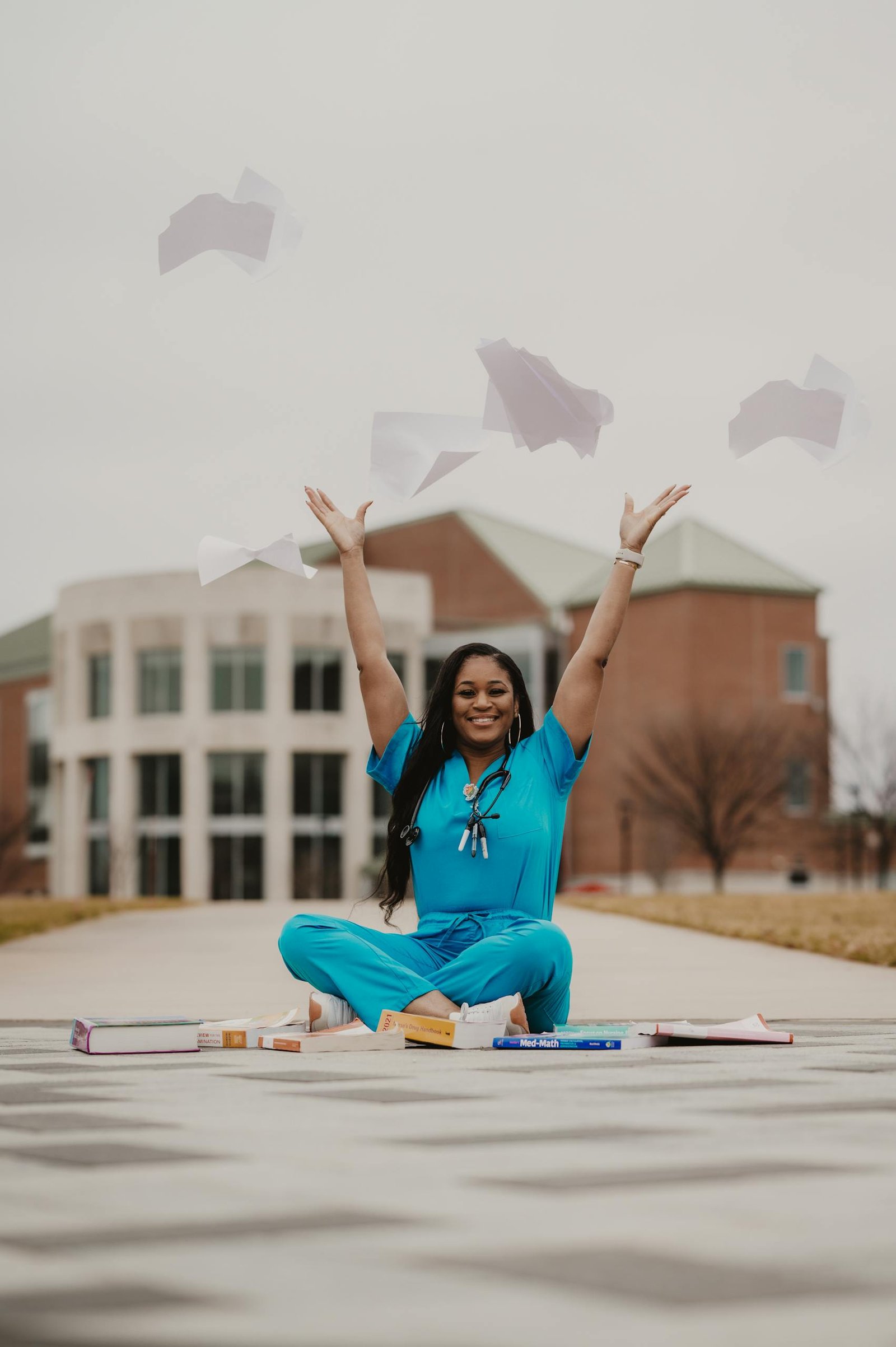 Happy medical student in blue scrubs celebrates graduation by tossing papers outdoors.